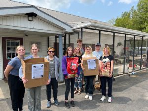 group of students stand at the animal shelter entrance with donation boxes