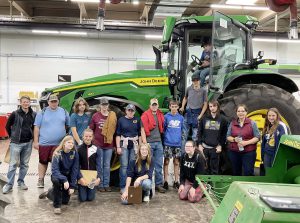 group of students and staff stand in front of a large John Deere tractor