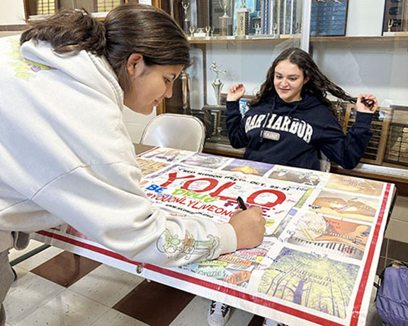 A student signs a banner as another student witnesses it