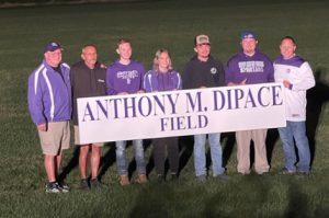 seven people stand in a field holding a sign saying Anthony M. DiPace Field 