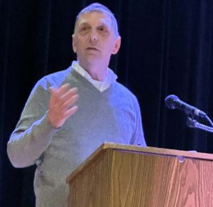 man wearing sweater speaks at podium