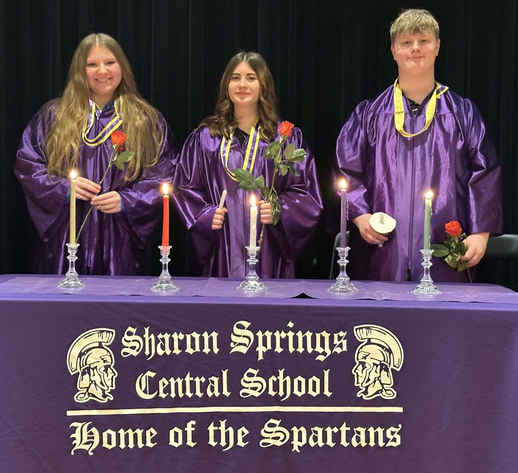 three new national honor society inductees dress in gowns with candles