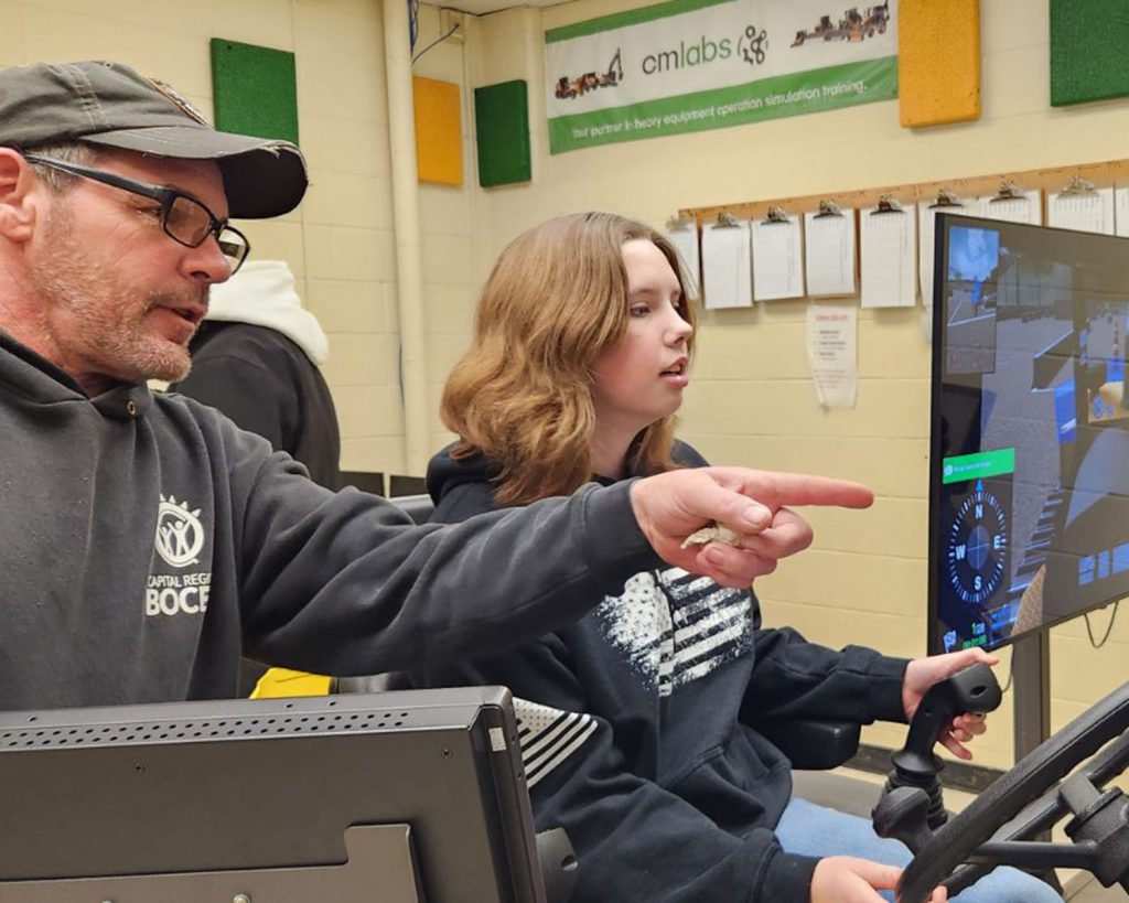 Girls works with teacher on a heavy equipment simulator