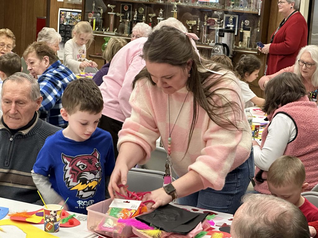 teacher works with students on a craft project