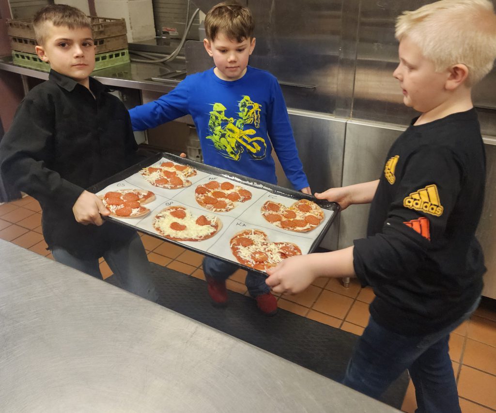 three boys take a tray out of the oven