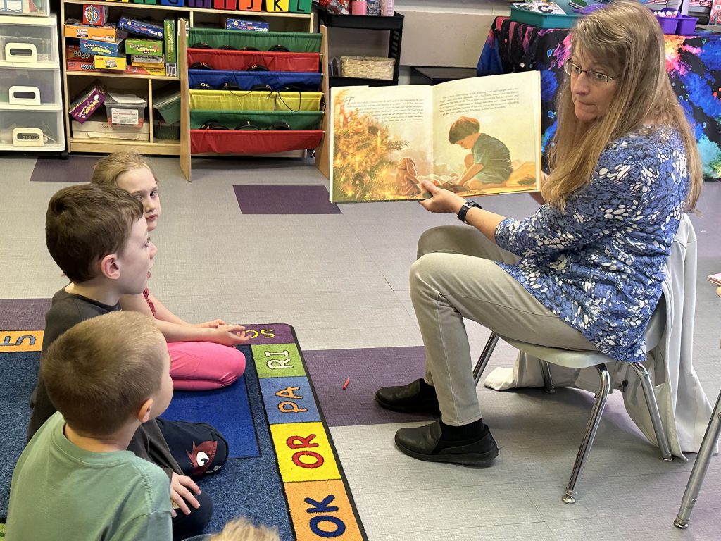 woman reads a book to a group of young children sitting on the floor