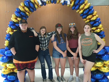 five student pose in front of horseshoe of balloons