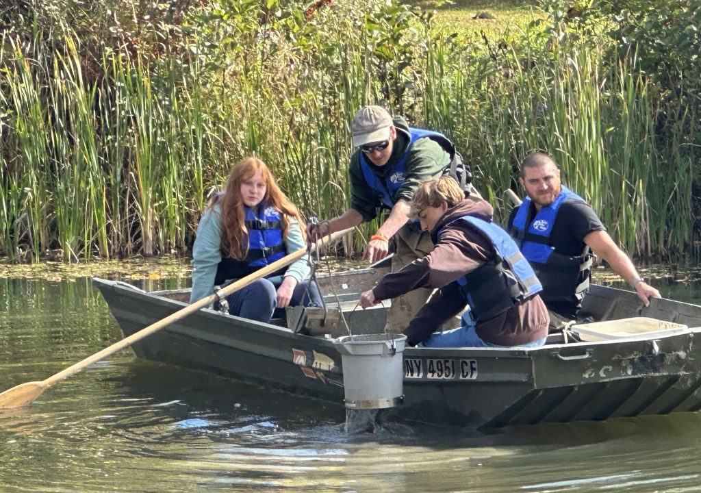 students collect pond samples from a row boat with a bucket