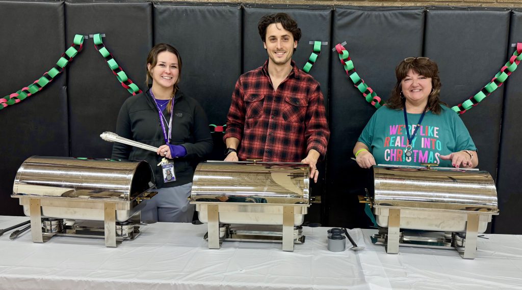 three faculty members prepare to serve out food from containers
