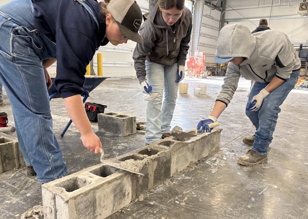 three students work on a masonry project