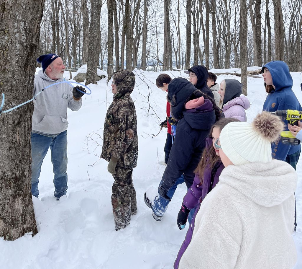 students watch as farm taps a maple tree