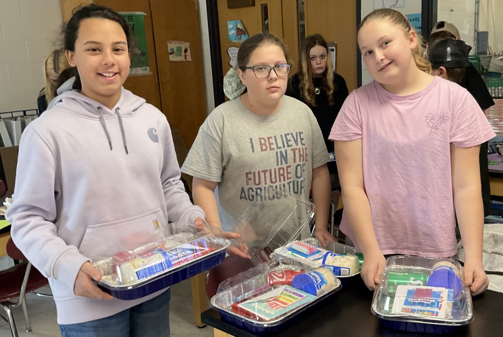 three students display the birthday cake kit they create to donate to the food pantry